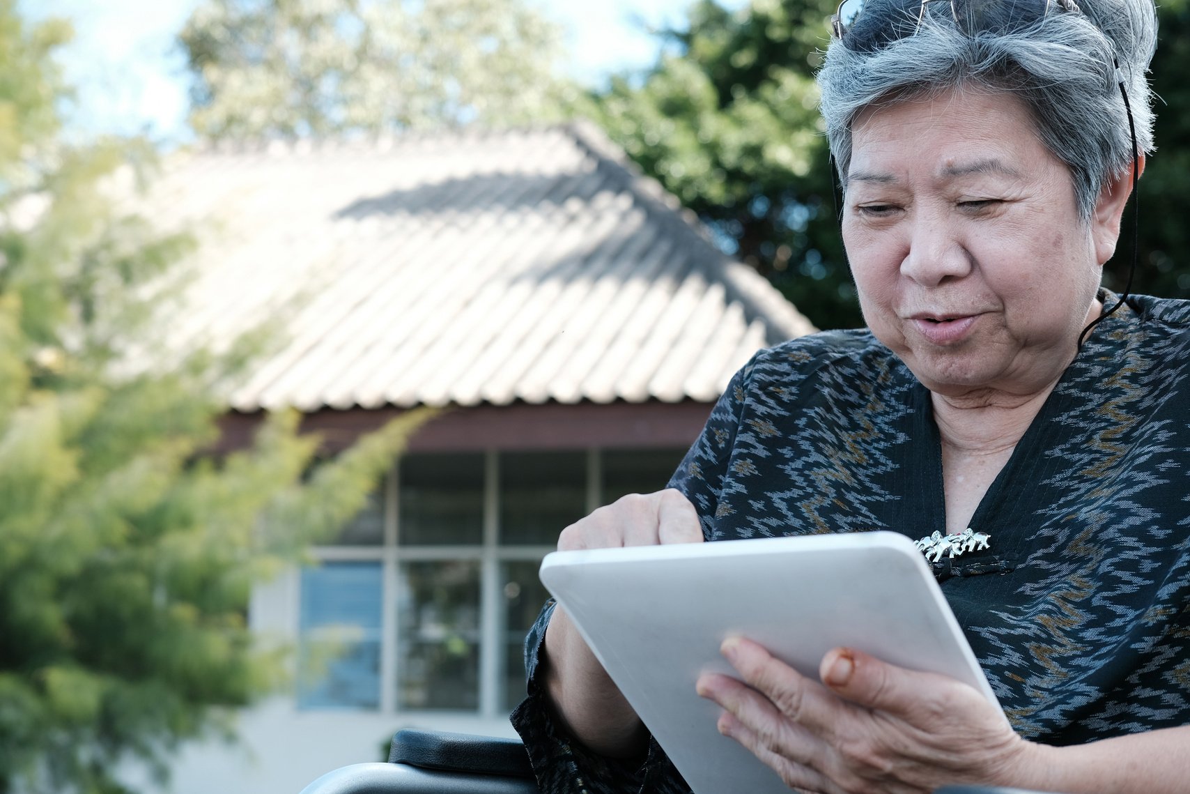 Elderly Asian Woman On A Wheelchair Using Tablet